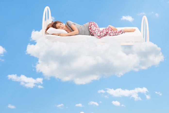 Mladá žena spí na posteli plující na mraku v nebesích