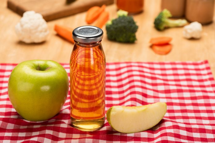 Jablko položené na stole vedle sklenice s jablečnou šťávou.