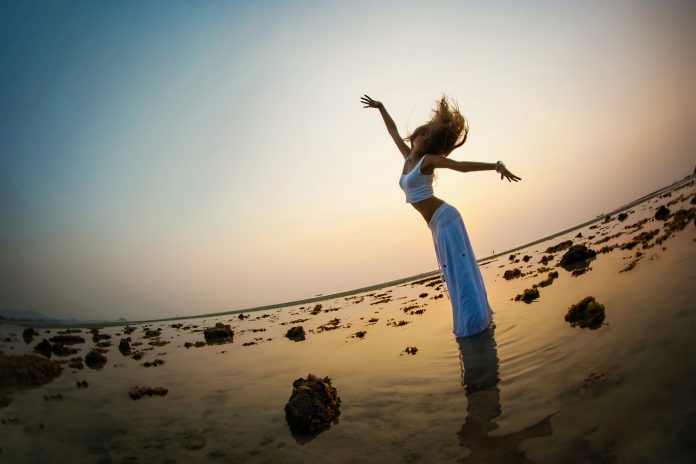 Krásná žena tančí v západu slunce na pláži.